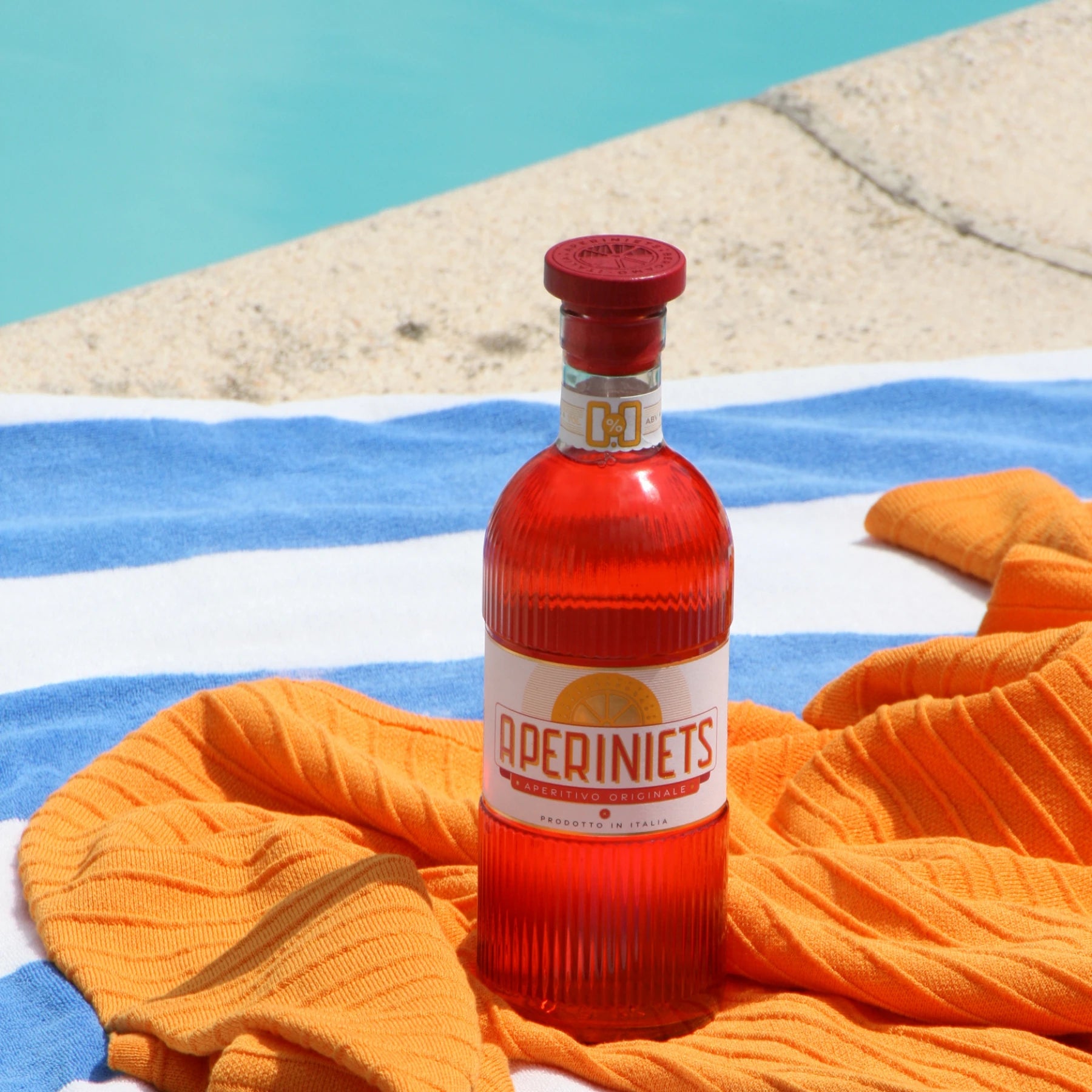 Aperiniets alcohol-free aperitif bottle on a towel by the pool in a summer lifestyle setting.