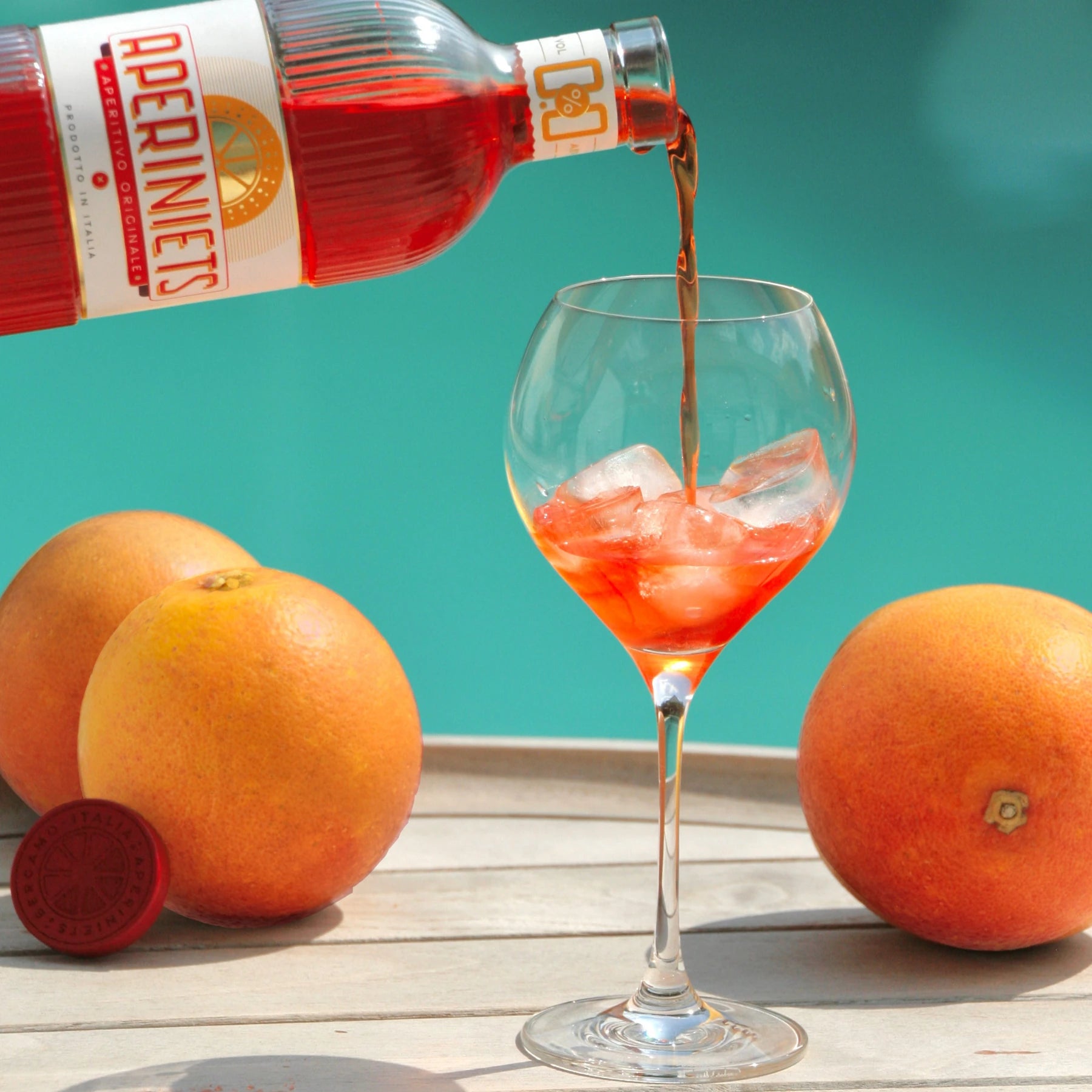 Aperiniets alcohol-free aperitif being poured into a glass with ice and oranges for a spritz serve.