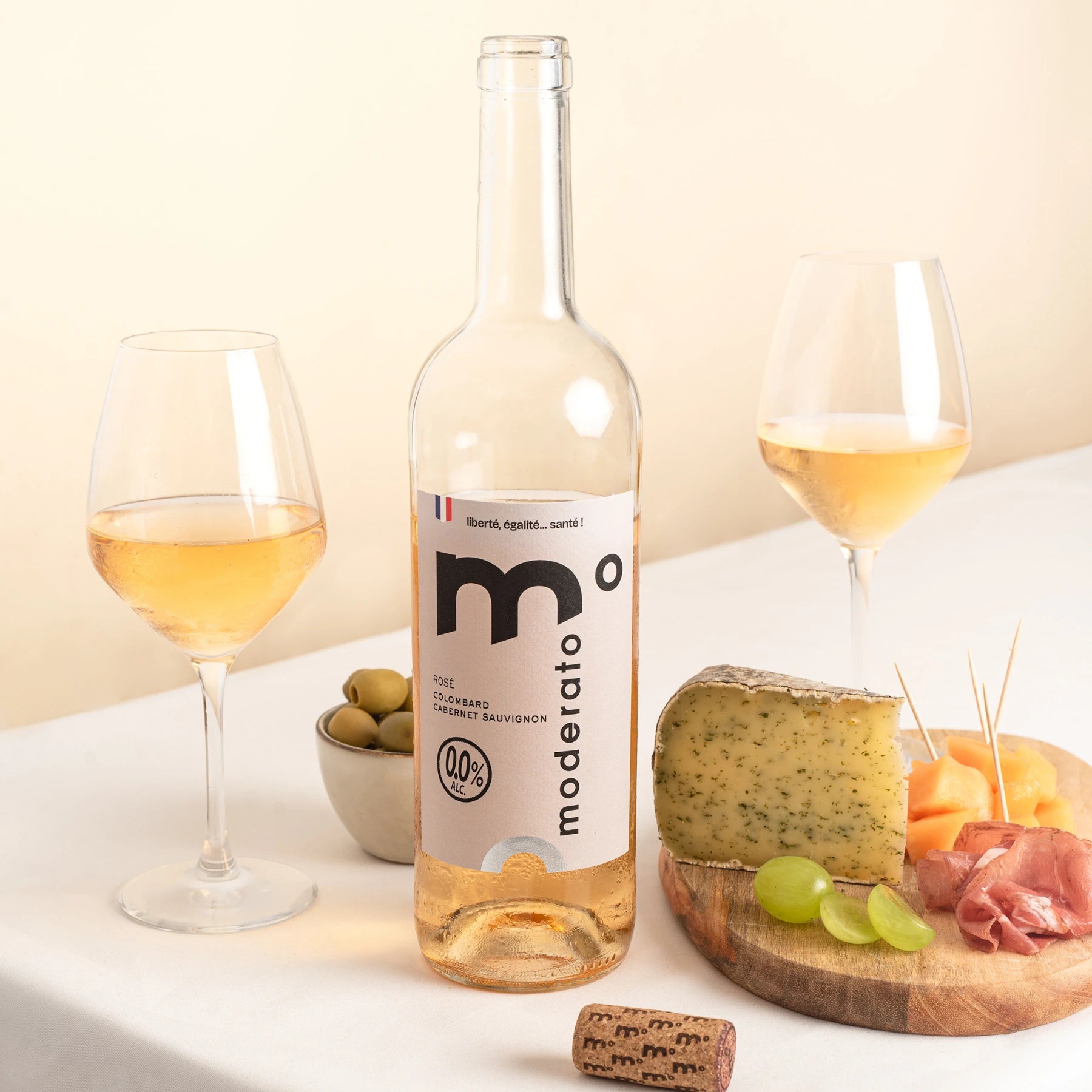 Moderato alcohol-free rosé wine paired with cheese, olives and fruit, clean studio composition.
