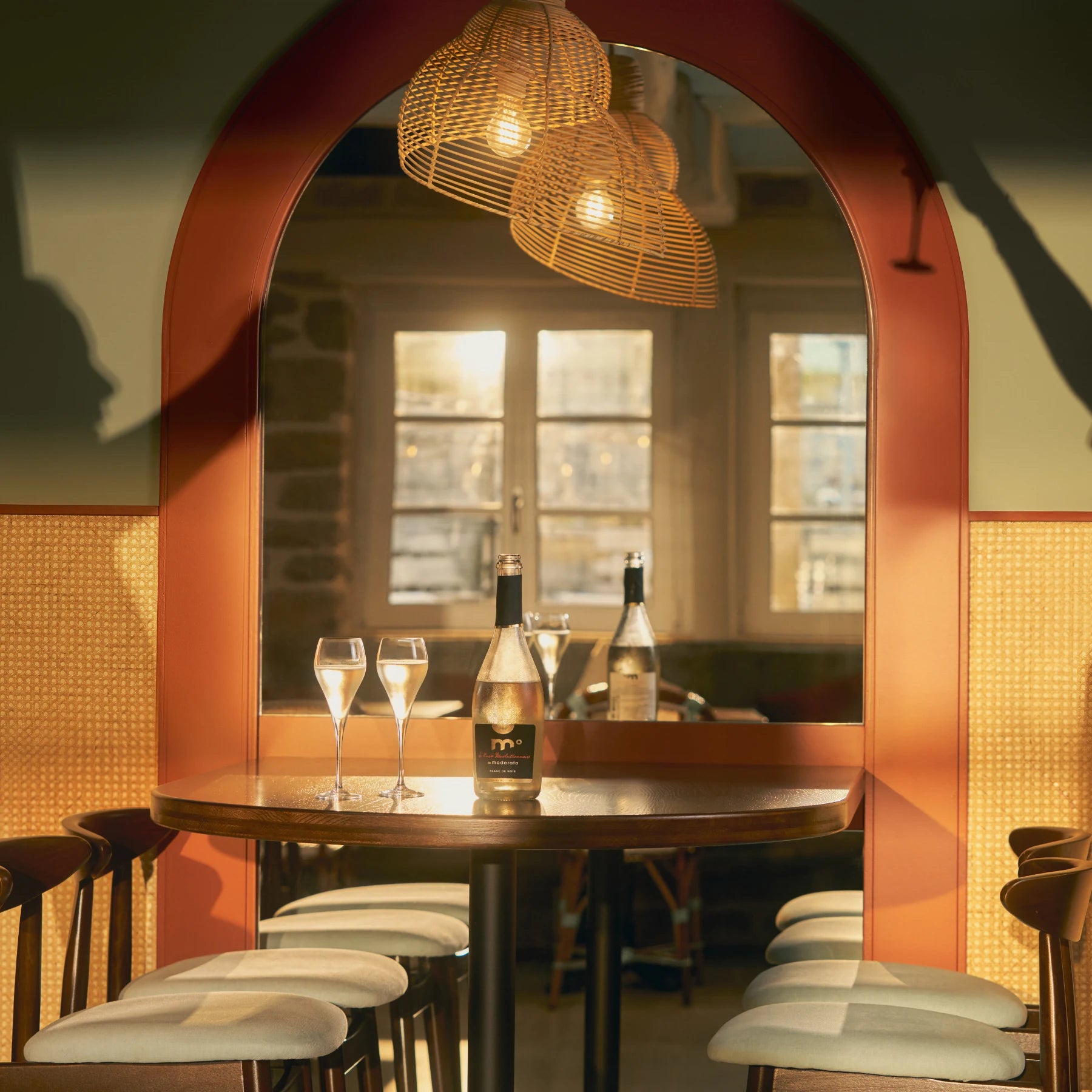Moderato alcohol-free Blanc de Noir sparkling wine from Merlot served in a warm restaurant setting with two glasses.