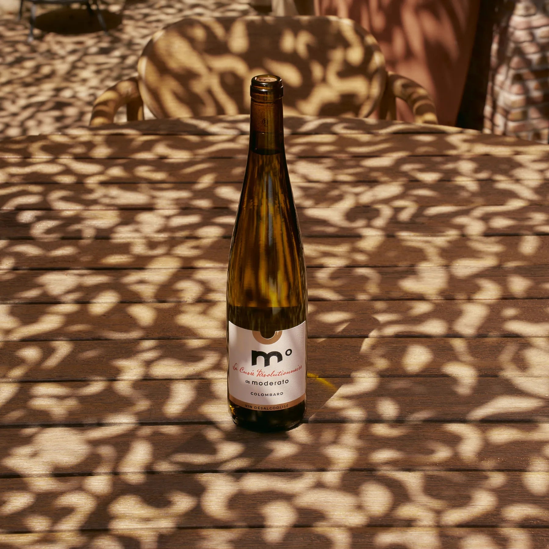 Moderato Cuvée Révolutionnaire Colombard alcohol-free white wine bottle on sunlit outdoor table with shadows