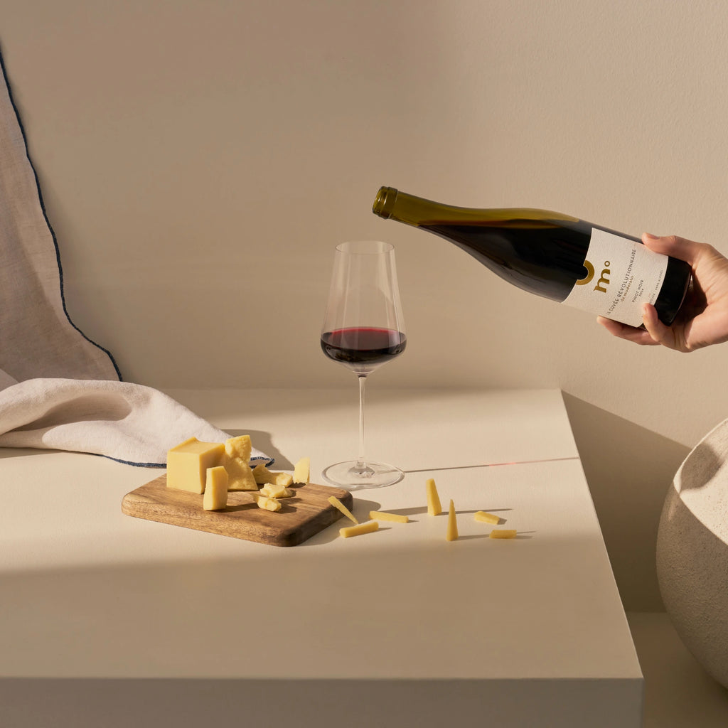Moderato alcohol-free Pinot Noir red wine being poured into a glass with cheese on a wooden board.