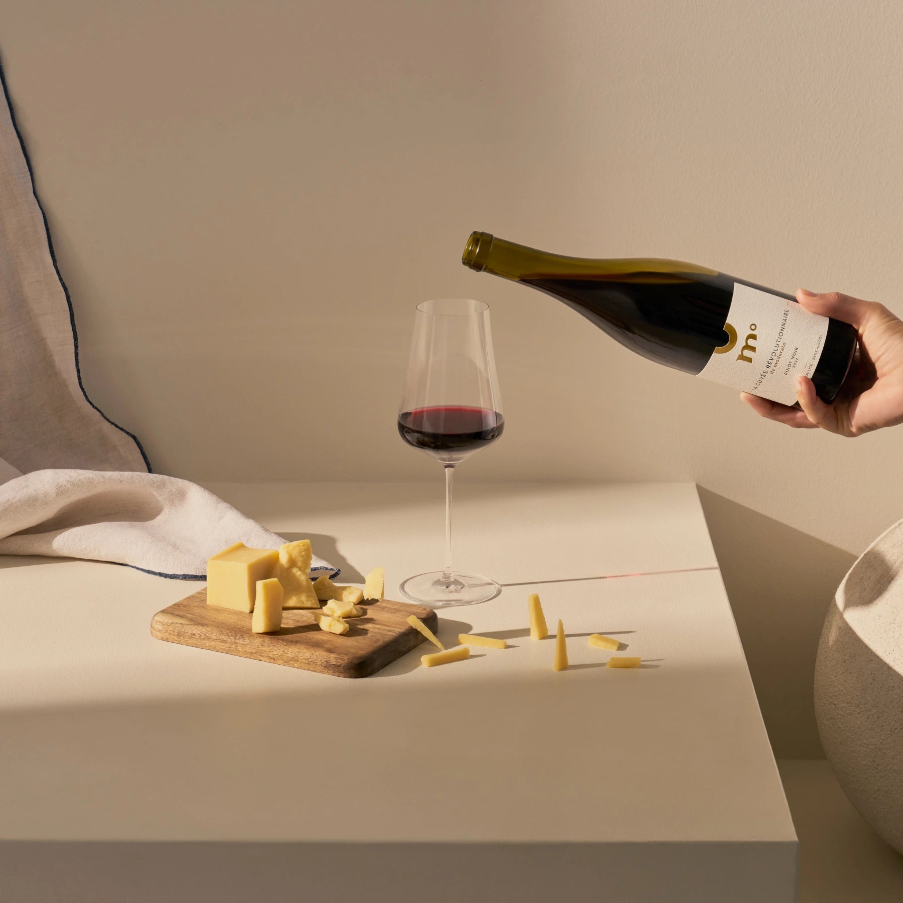 Moderato alcohol-free Pinot Noir red wine being poured into a glass with cheese on a wooden board.