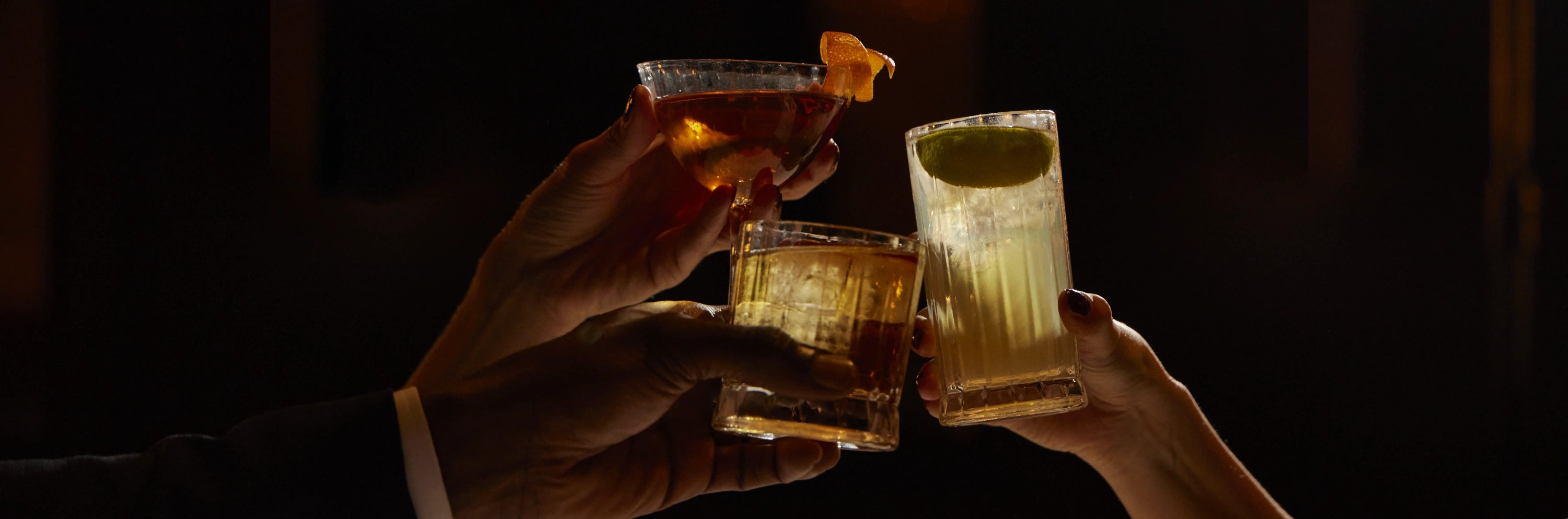 Three alcohol-free cocktails raised in a toast, served in elegant glassware against a dark, atmospheric background.