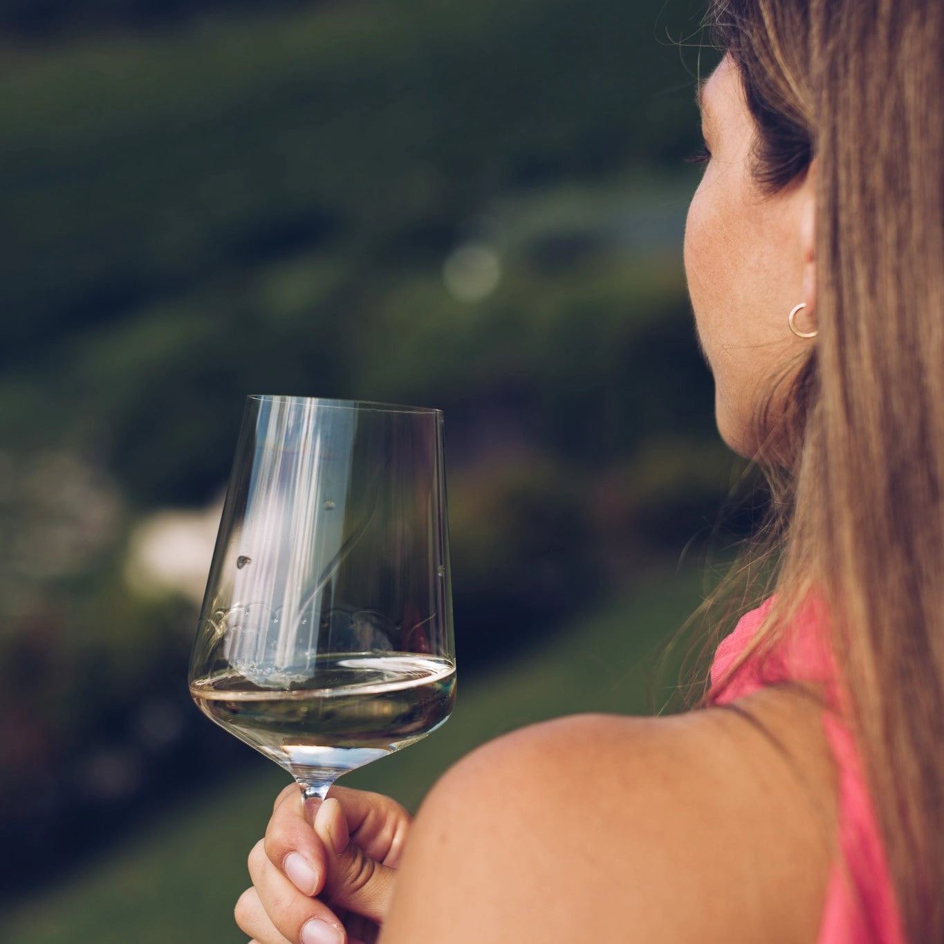 Alcohol-free white wine in glass held outdoors in natural setting.