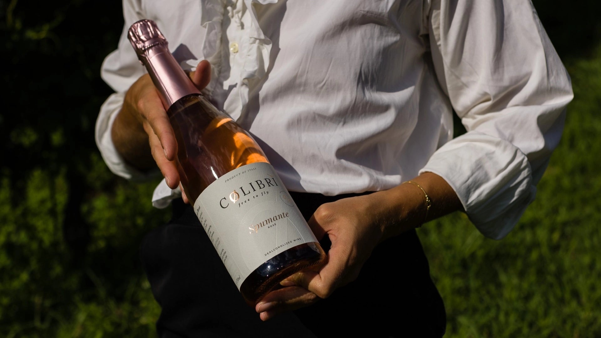 Person holding a bottle of Colibrì Spumante Rosé alcohol-free sparkling wine outdoors.