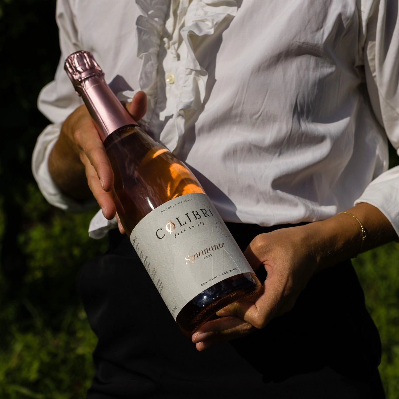 Colibri Spumante Rosé alcohol-free sparkling wine held in hand outdoors.