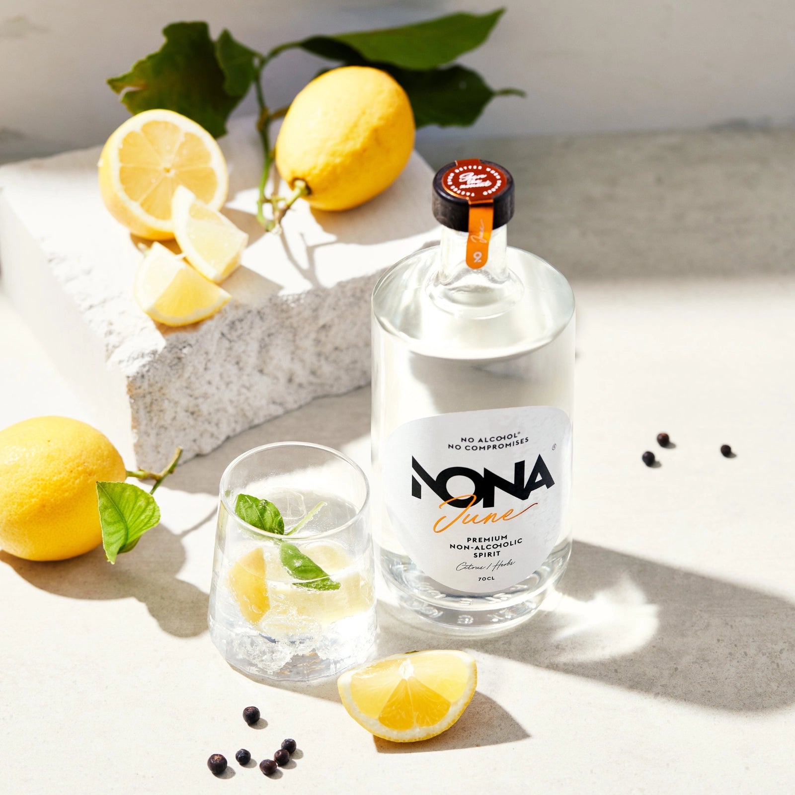 Bottle of Nona June with a glass of ready mocktaile on a light surface with lemons and blackberries.