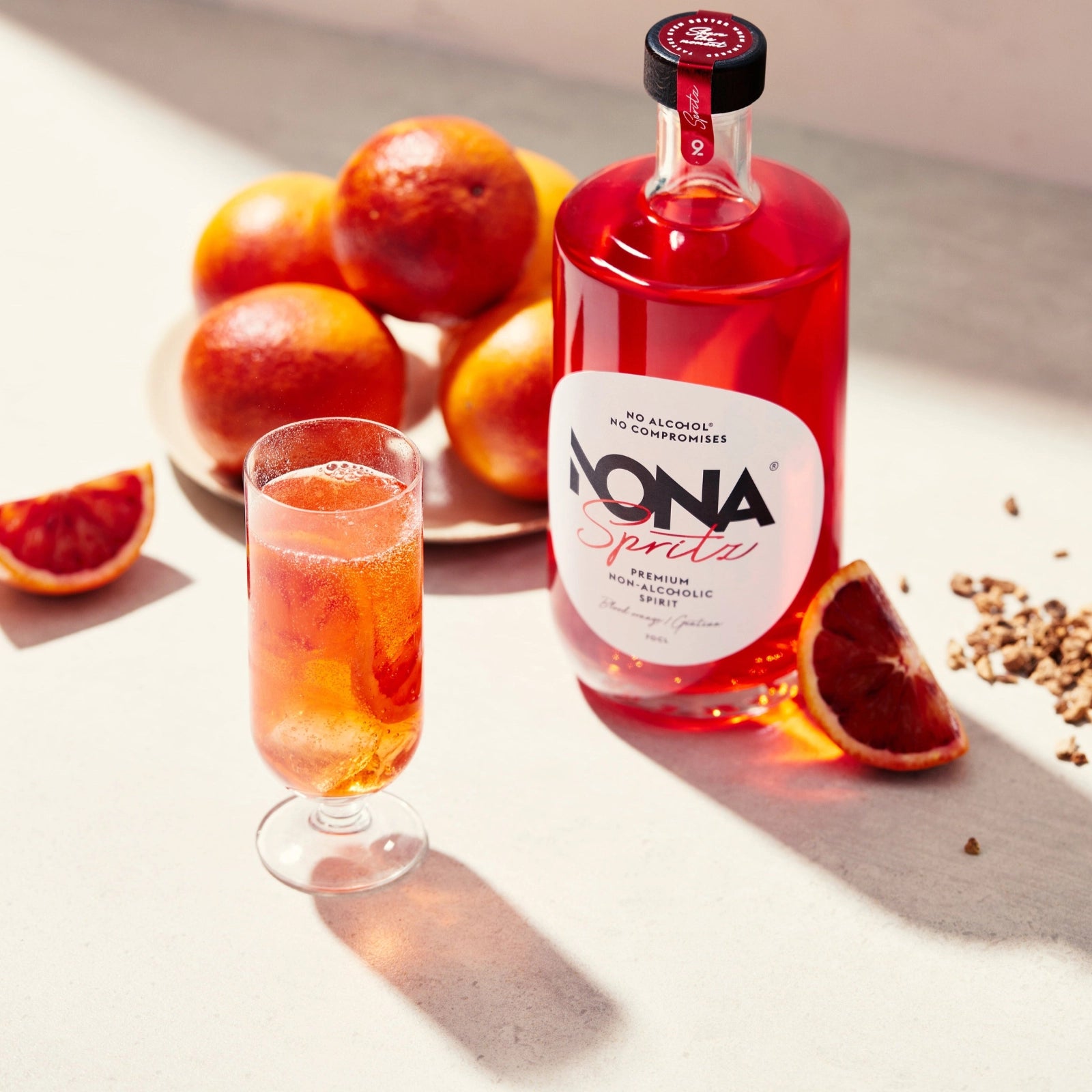 Bottle of NONA Spritz with a glass NONA SPRITZ WITH TONIC drink and blood oranges on a light surface