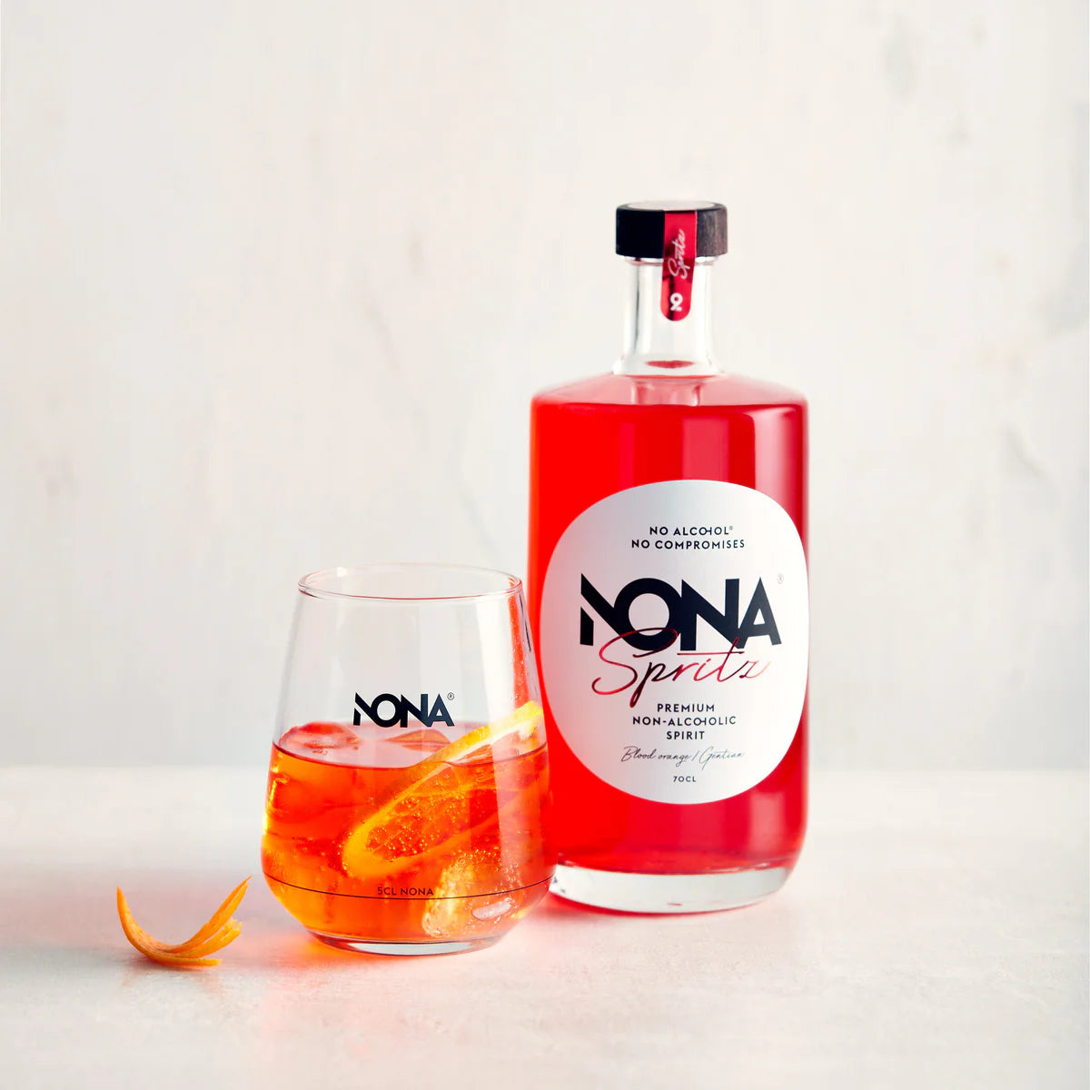 700 ml Bottle of NONA Spritz and glass of NONA Spritz and Tonic mocktail on a light background