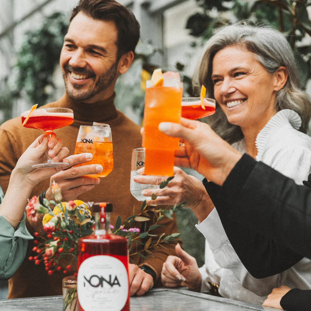 Smiling adults toasting with colorful NONA drinks at a table.
