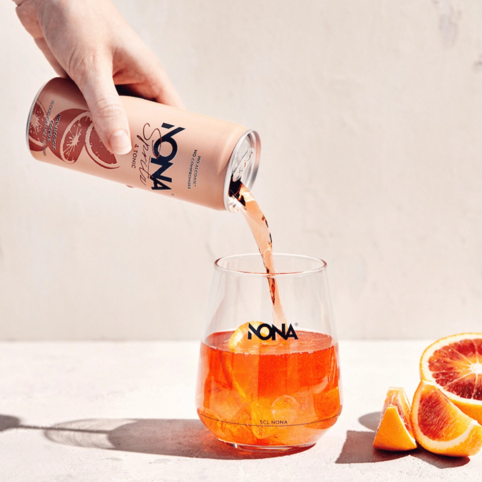 NONA Spritz & Tonic alcohol-free cocktail being poured from the can into a glass with ice and orange slices