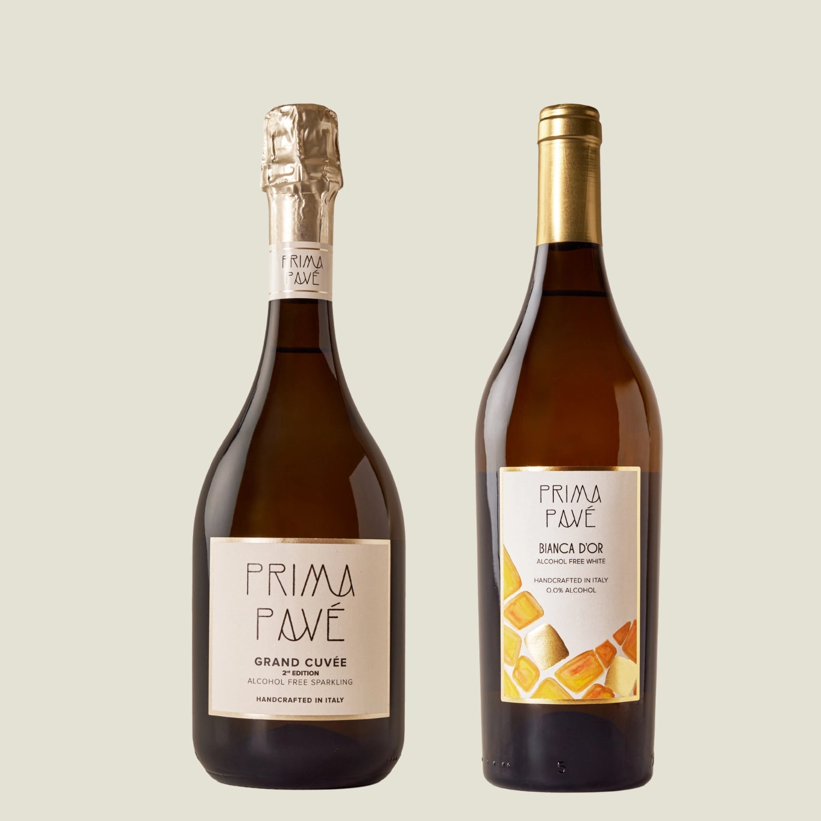 Two bottles of Prima Pavé non-alcoholic wine — Grand Cuvée sparkling and Bianca D'Or white — on a neutral background.