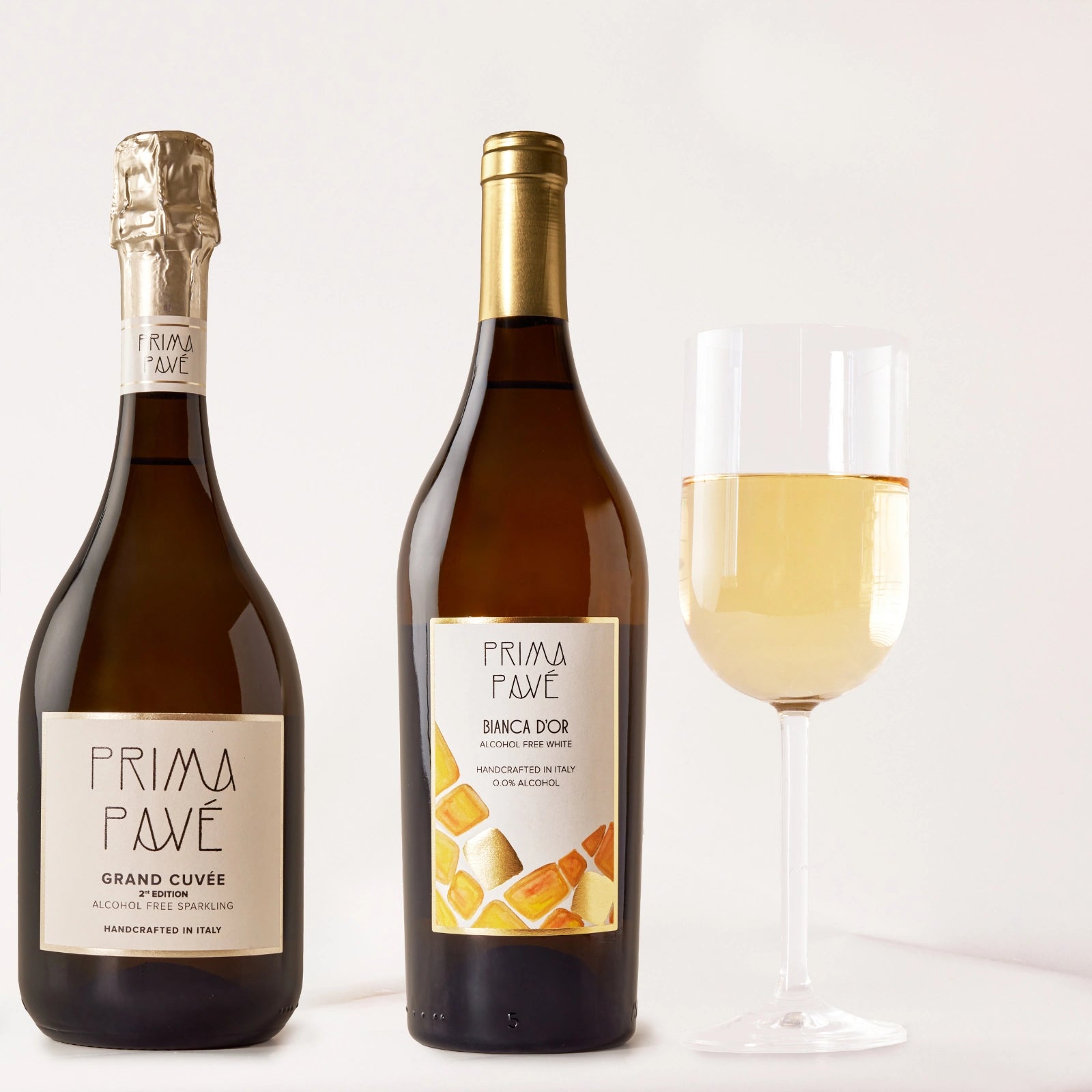 Prima Pavé Grand Cuvée and Bianca D'Or non-alcoholic wines displayed with a filled wine glass in a clean studio setting.