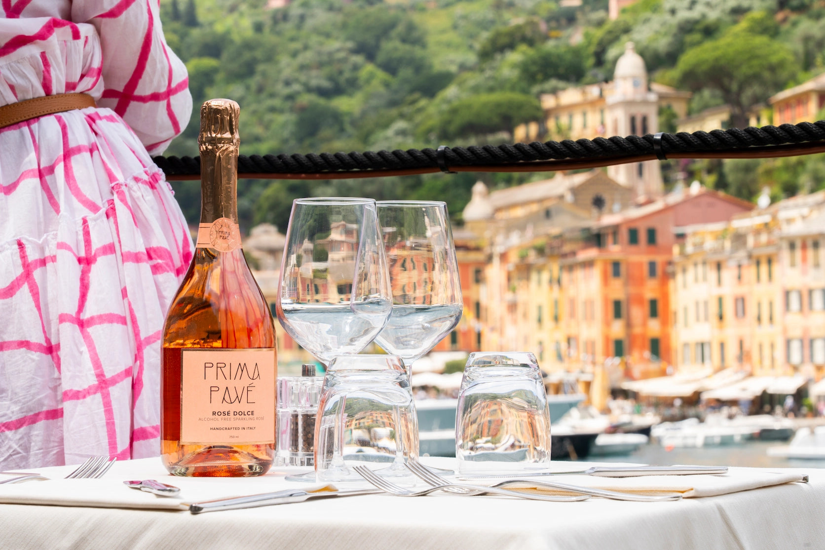 Prima Pavé Rosé Dolce alcohol-free sparkling wine on an elegant outdoor table overlooking colorful Portofino buildings, with wine glasses and a summer setting.