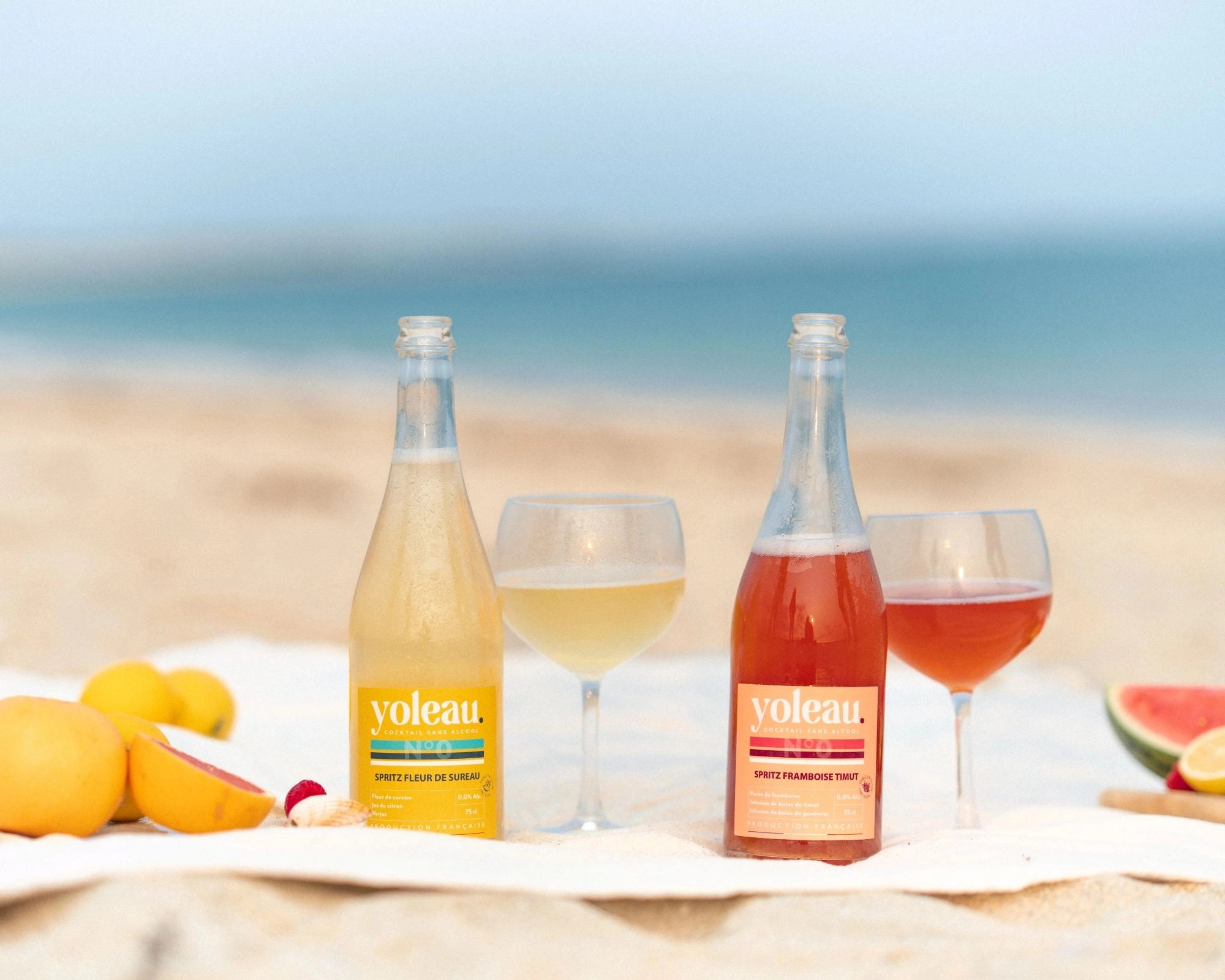 Yoleau alcohol-free spritz mocktails on the beach with citrus fruit and glasses, summer aperitif scene by the sea.