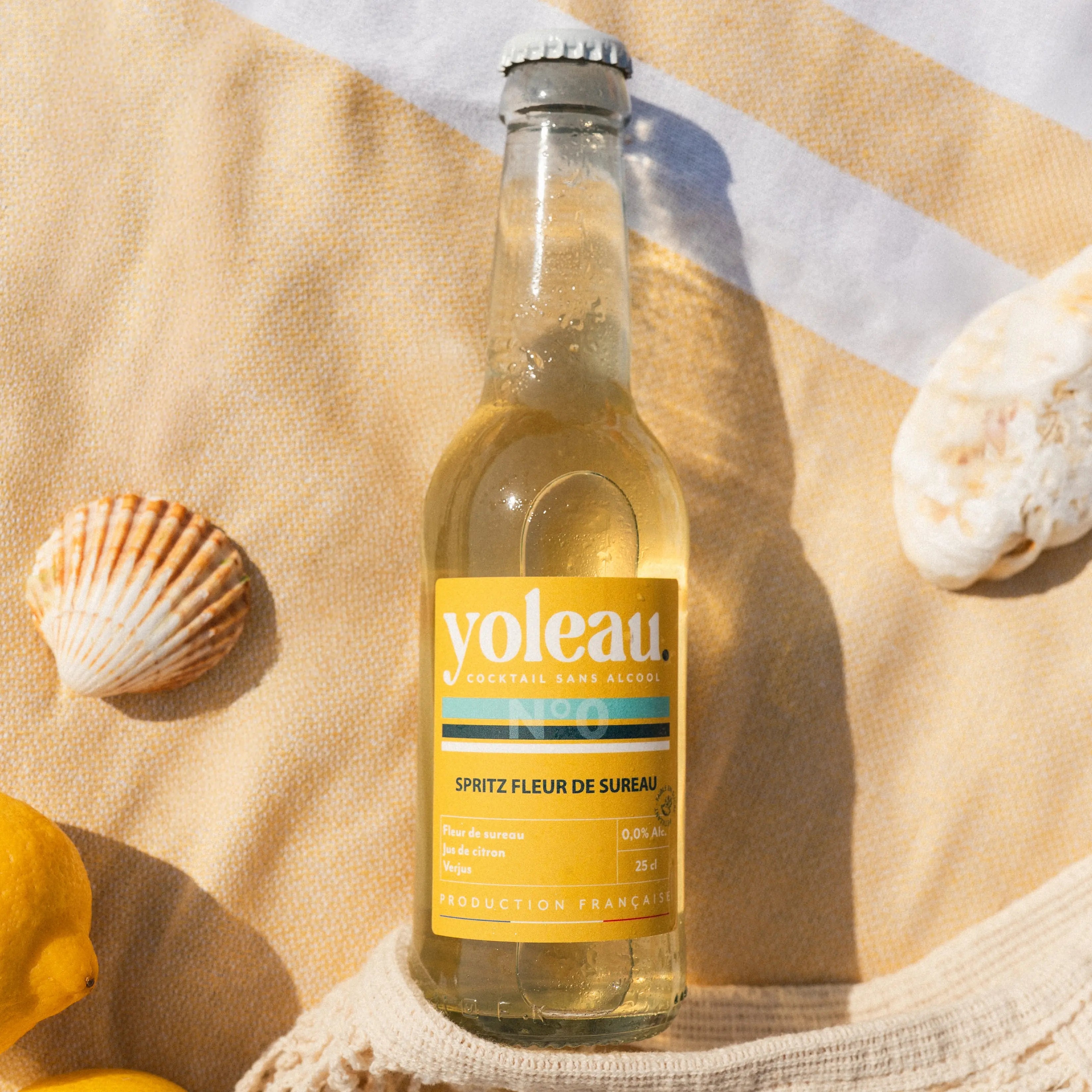 Bottle of Yoleau elderflower spritz mocktail 250ml alcohol-free drink on a beach towel with lemons.