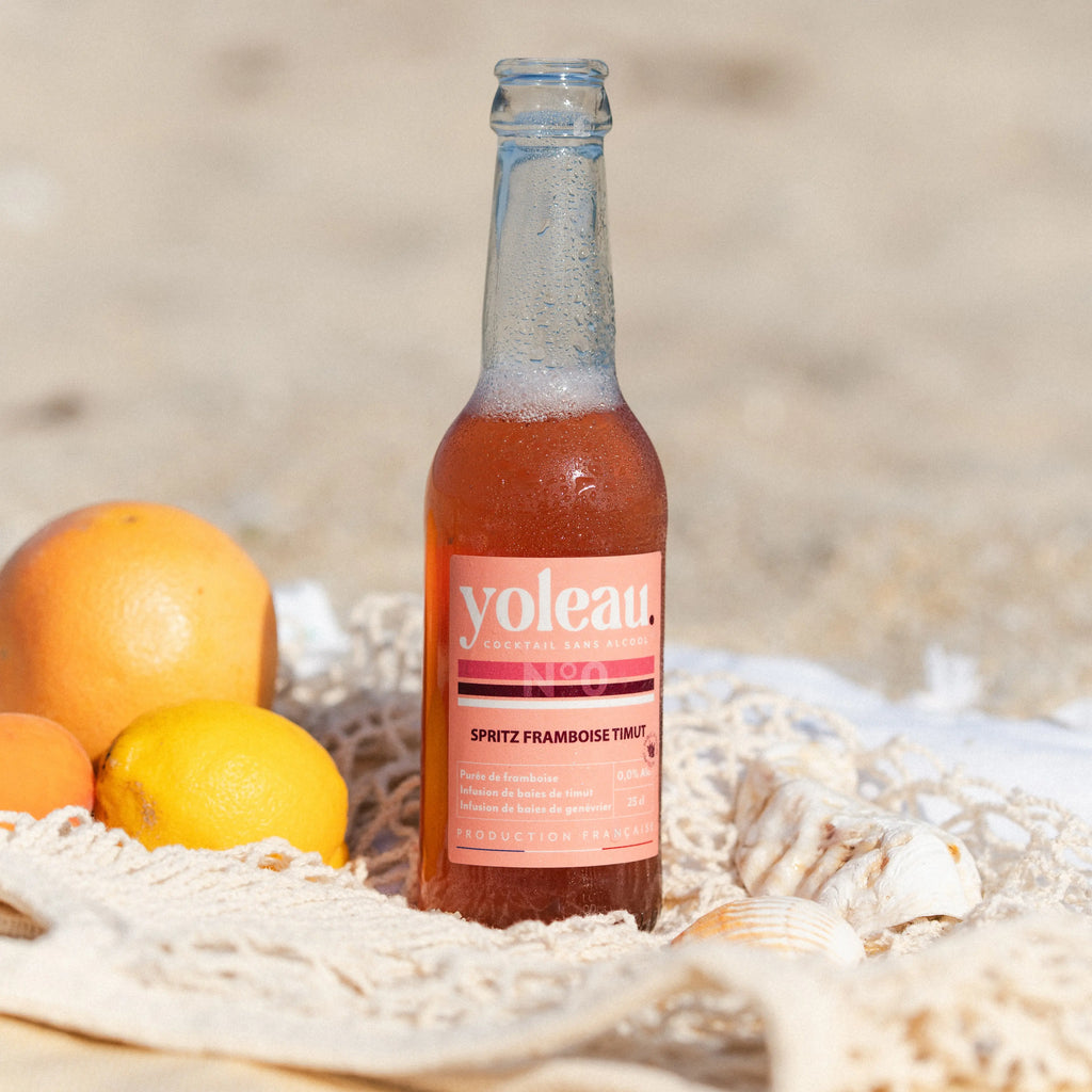 Yoleau Raspberry Spritz mocktail 0.0% alcohol-free drink bottle 250 ml on the beach with citrus fruits.