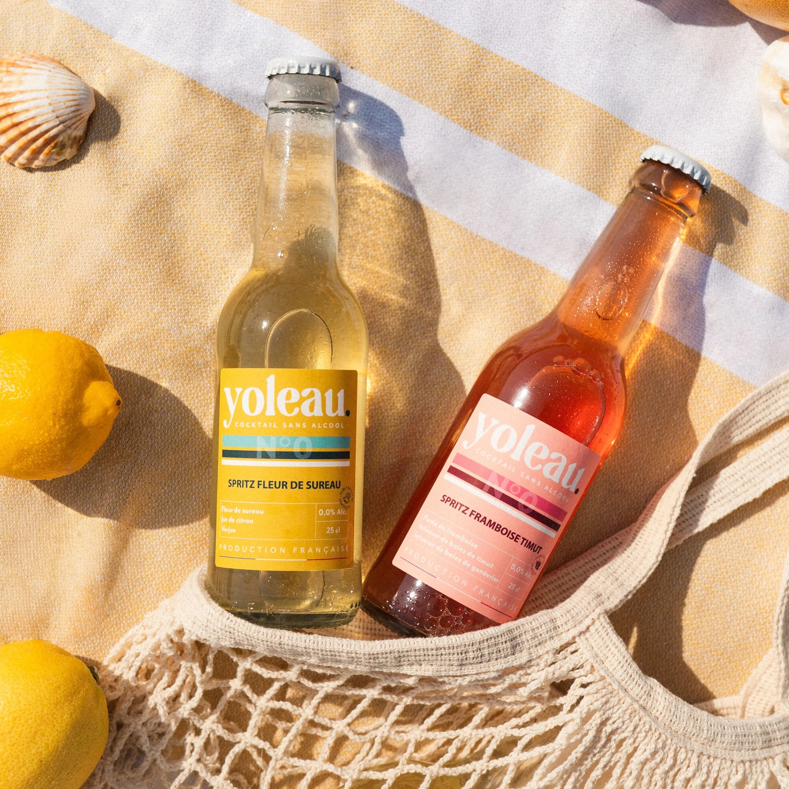 Yoleau alcohol-free spritz mocktails raspberry and elderflower 0.0% 250 ml bottles on a beach towel with lemons.