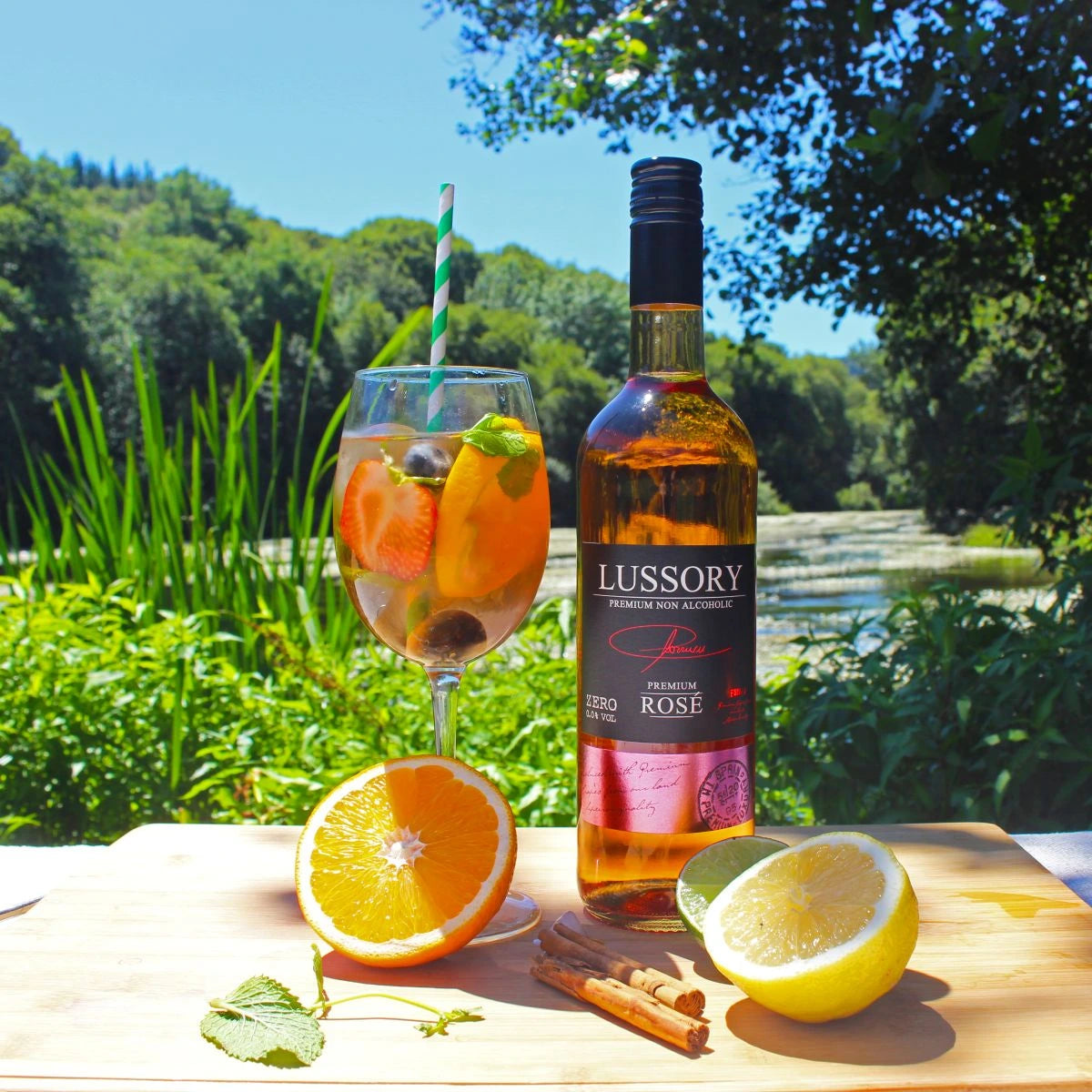 LUSSORY Premium Rosé Non-Alcoholic Wine bottle with a glass of rosé garnished with fresh fruit and citrus slices, served outdoors by the water