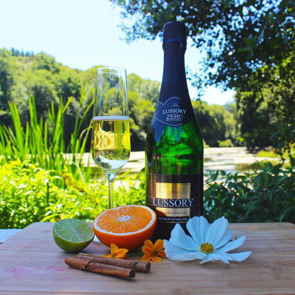 LUSSORY Premium Sparkling Non-Alcoholic White Wine bottle with a flute of golden bubbles, surrounded by citrus fruits and flowers in a sunny outdoor setting.