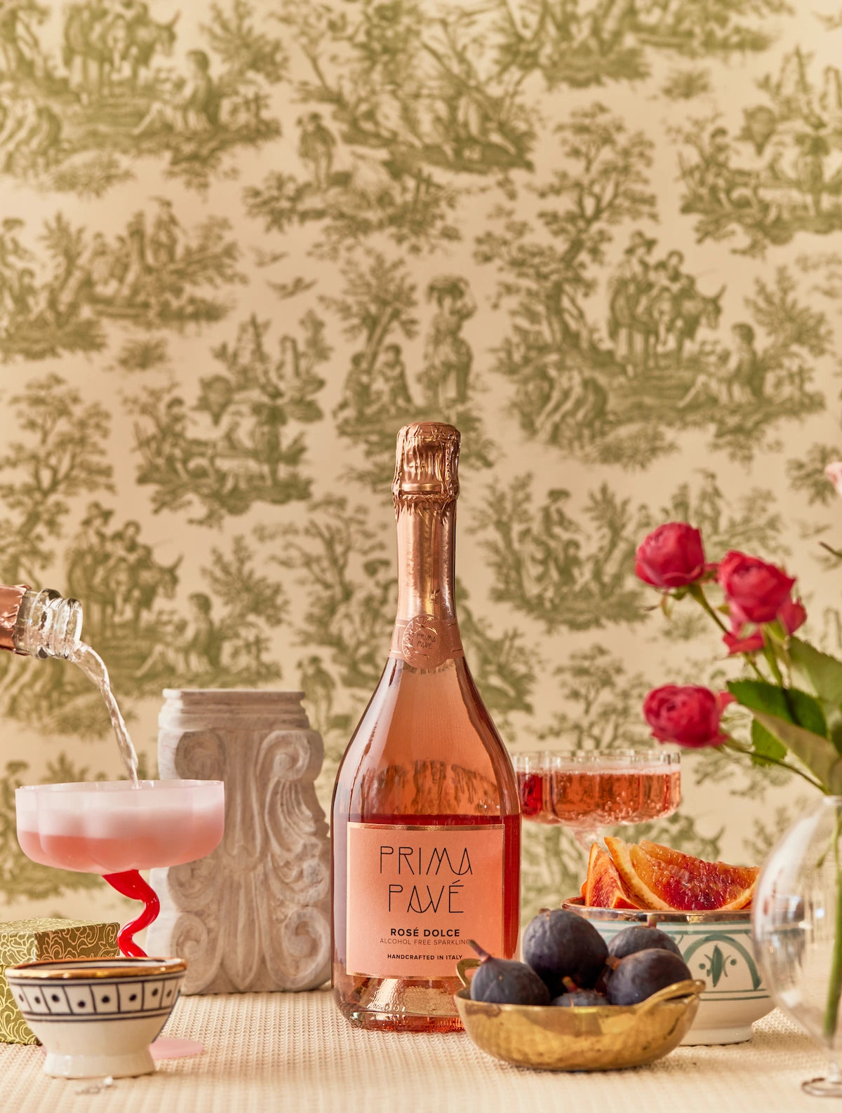 PRIMA PAVÉ Rosé Dolce Non-Alcoholic Sparkling Wine bottle with coupe glass, figs, and pink roses on a vintage Italian-style background.