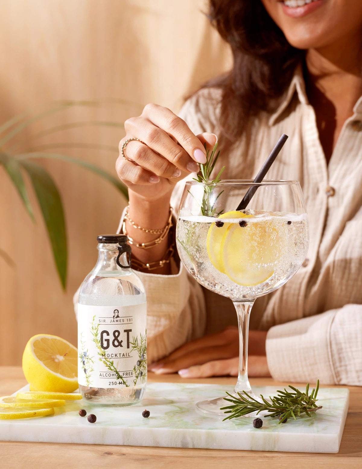 SIR. JAMES 101 Gin Tonic Alcohol Free 250 ml bottle and glass served with lemon slices and rosemary, held by a smiling woman in a warm natural setting