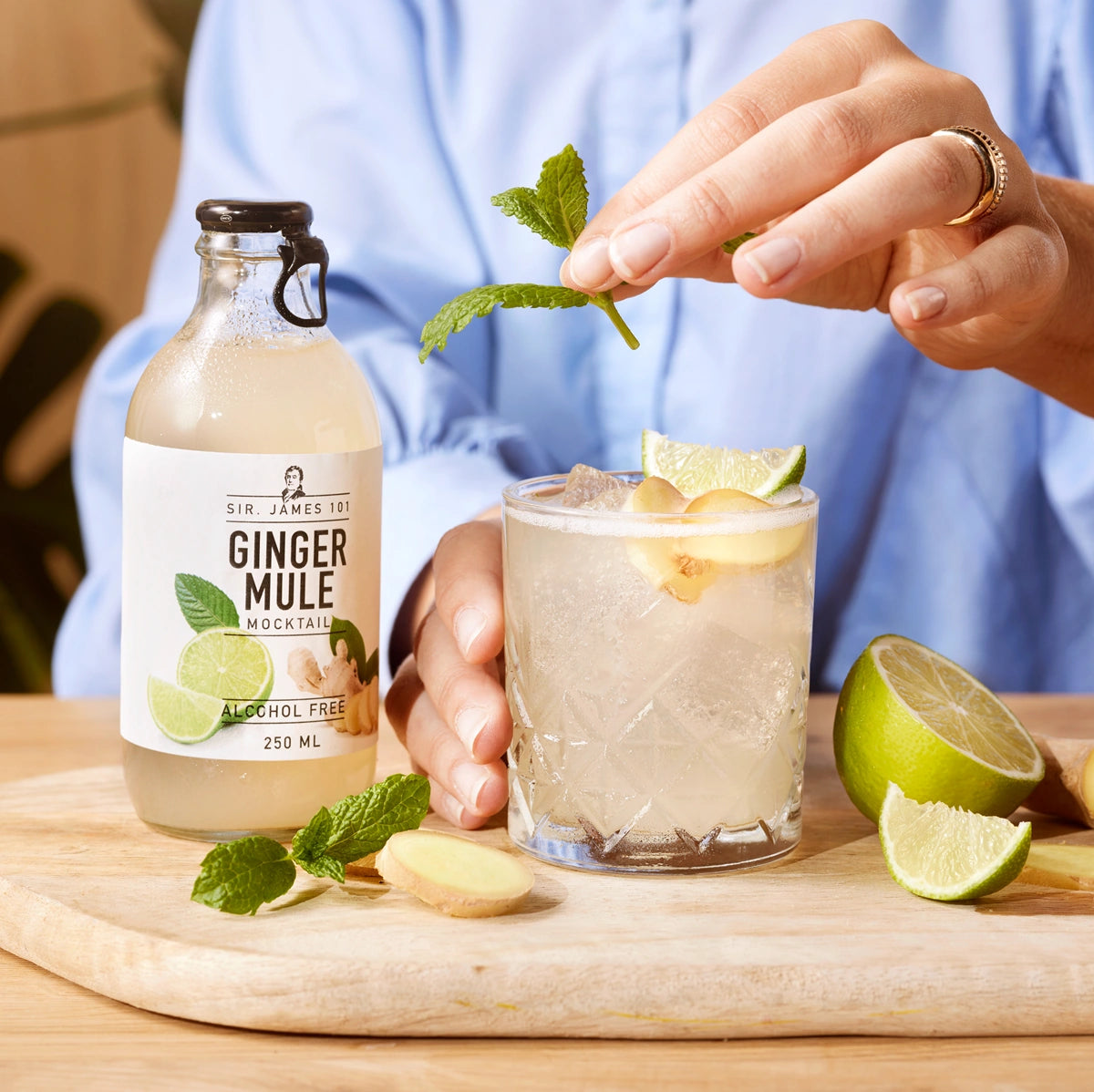 SIR. JAMES 101 Ginger Mule Alcohol Free 250 ml bottle with a glass of alcohol-free ginger cocktail garnished with lime, mint, and fresh ginger on a wooden table.