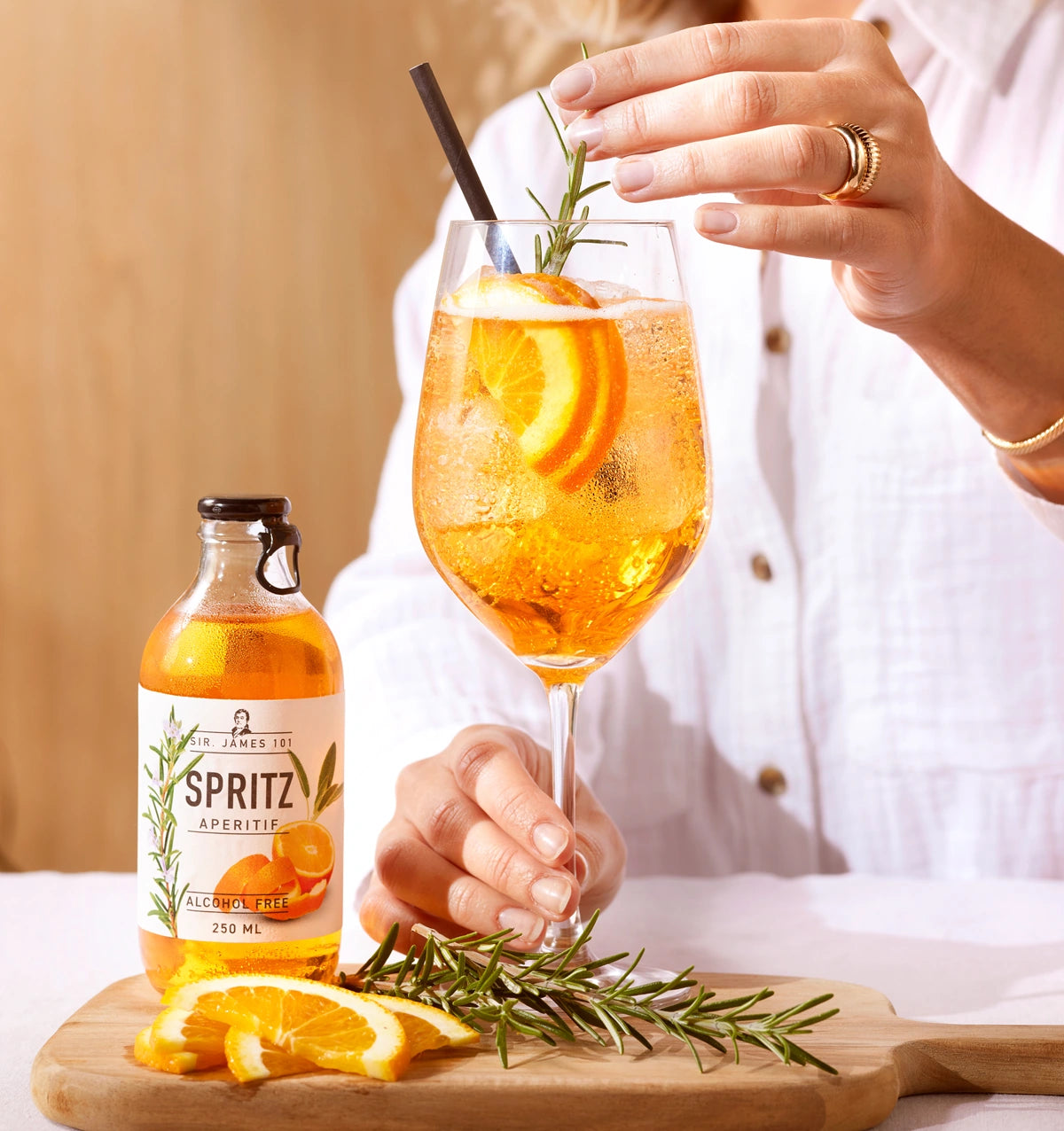 SIR. JAMES 101 Spritz Aperitif Alcohol Free 250 ml bottle with glass of orange mocktail garnished with rosemary, orange and ice on a wooden board.